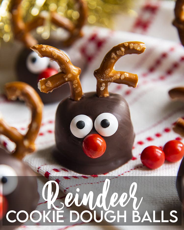 A cookie dough ball decorated to look like a reindeer with candy eyes, a red nose, and pretzel antlers.