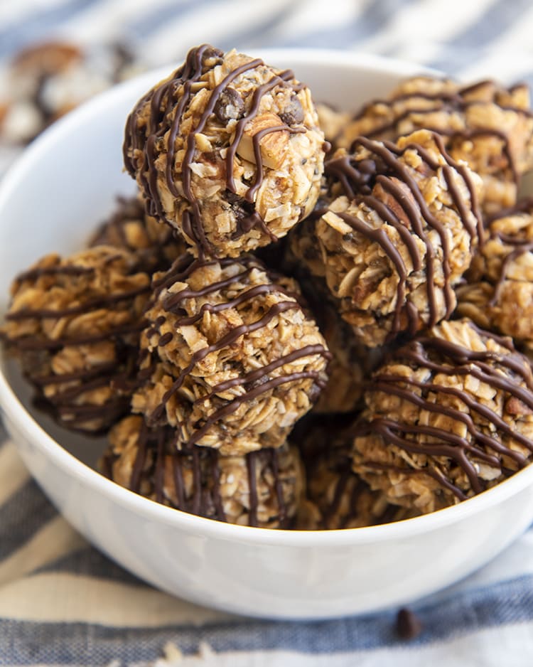 A bowl of almond joy energy bites, that are oat balls, with mini chocolate chips, almonds, and drizzled in chocolate on top.