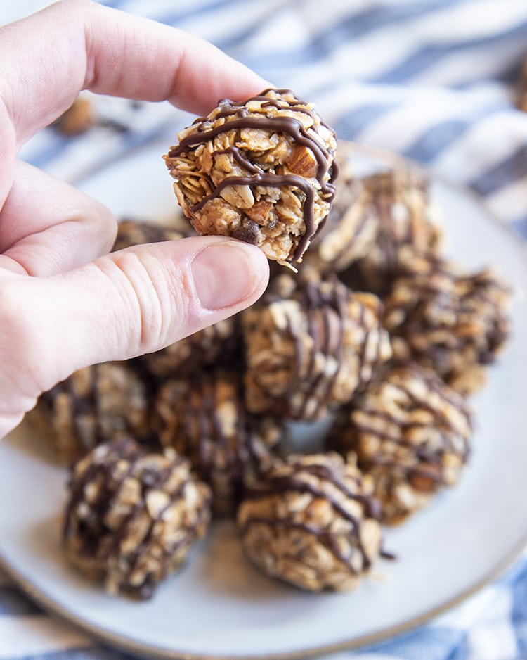 A hand holding an almond joy granola ball over a pile of them on a plate.