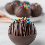 A chocolate sphere, drizzled with chocolate on top and topped with chocolate rainbow chip pieces.