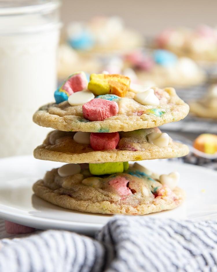 A stack of three lucky charms cookies on a small white plate. Each cookie is topped with the marshmallows from lucky charms cereal.