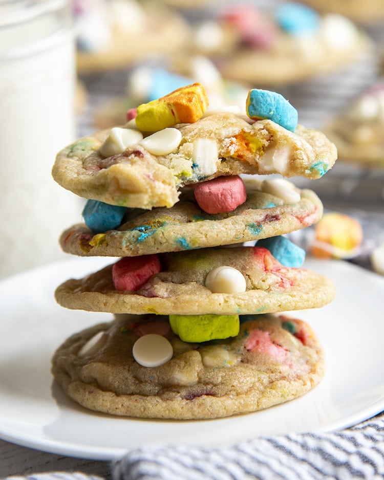 A stack of 4 cookies full of white chocolate chips and lucky charms marshmallows on a white plate.