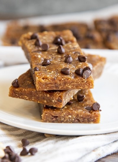 A stack of 3 homemade peanut butter chocolate chip larabars on a small plate with mini chocolate chips showing on the top one.