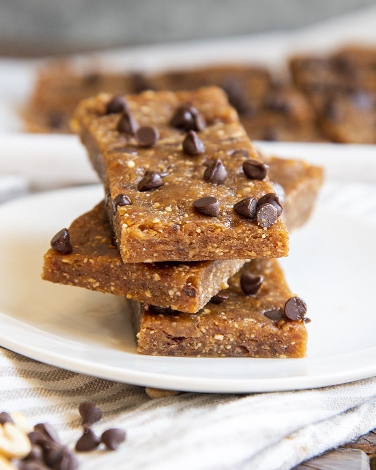 A stack of 3 homemade peanut butter chocolate chip larabars on a small plate with mini chocolate chips showing on the top one.
