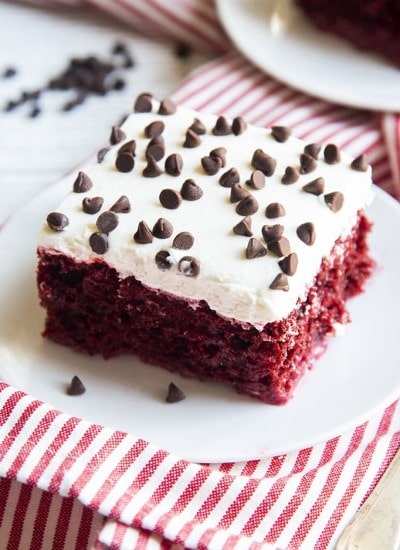 A square piece of red cake topped with a white cream cheese frosting, and topped with mini chocolate chips.