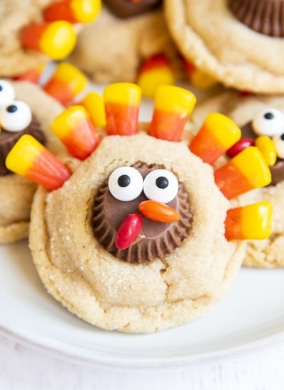 A close up shot of a peanut butter cookie decorated to look like a turkey with a peanut butter cup decorated with candy eyes, and chocolate covered candies for a beak, and candy corn at the top for feathers.