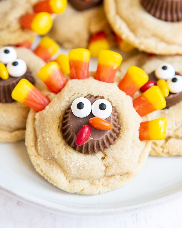A close up shot of a peanut butter cookie decorated to look like a turkey with a peanut butter cup decorated with candy eyes, and chocolate covered candies for a beak, and candy corn at the top for feathers.