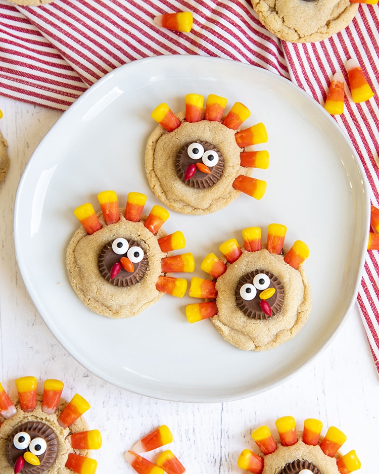 A white plate full of a pile of cookies decorated to look like turkeys with candy corn at the top, stuck into the cookies to look like feathers.