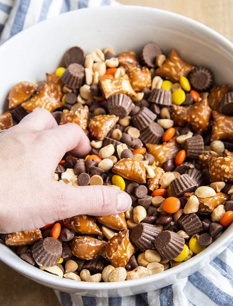 A hand reaching in to a bowl of a chocolate peanut butter snack mix.