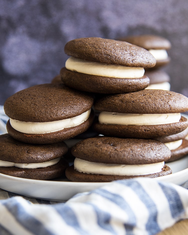 A stack of a plate of chocolate whoopie pies, the pile is three high with probably 8 cookie sandwiches in the stack.