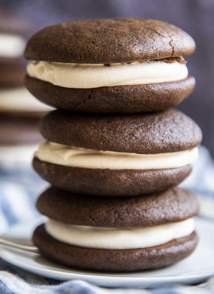 A stack of three chocolate whoopie pie sandwiches on a small plate, they are filled with a white marshmallow cream filling.
