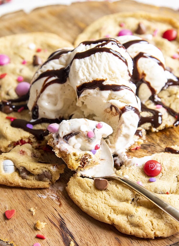 A big cookie topped with ice cream, and drizzled with chocolate sauce. A bite of the cookie and ice cream is on a fork.