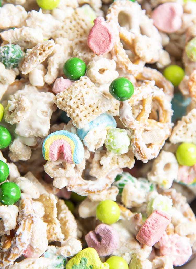 A close up of a snack mix with chex, pretzels, lucky charms, and green chocolate candies, all covered in white chocolate.