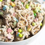 A close up of a a bowl of a lucky charms snack mix, with cereal, marshmallows, and green chocolate candies covered in melted white chocolate.