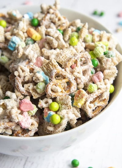 A close up of a a bowl of a lucky charms snack mix, with cereal, marshmallows, and green chocolate candies covered in melted white chocolate.