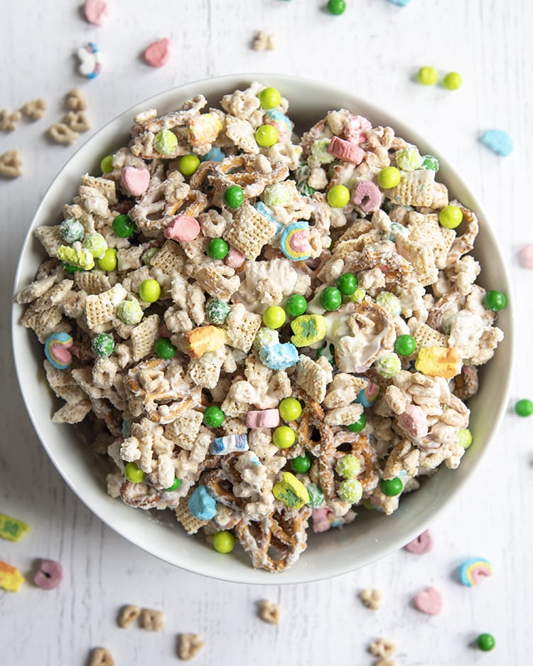 A bowl of a lucky charms snack mix, with cereal, marshmallows, and green chocolate candies covered in melted white chocolate.