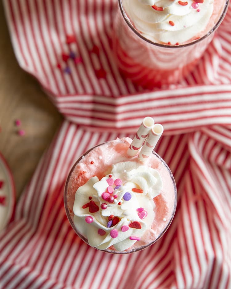 An overhead of two cups of a pink strawberry float topped with whipped cream.