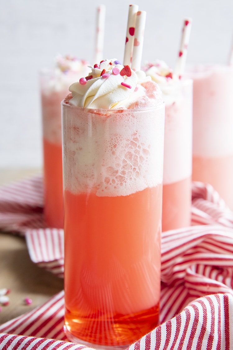 Tall glasses full of an orangey pink drink topped with whipped cream.