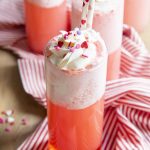 A tall glass cup filled with a pink drink, with foam on the top, and topped with whipped cream.