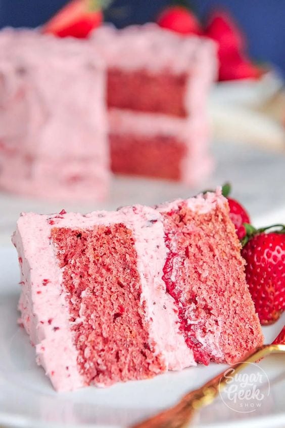 A slice of a double layered strawberry cake on a plate, with a pink strawberry frosting.