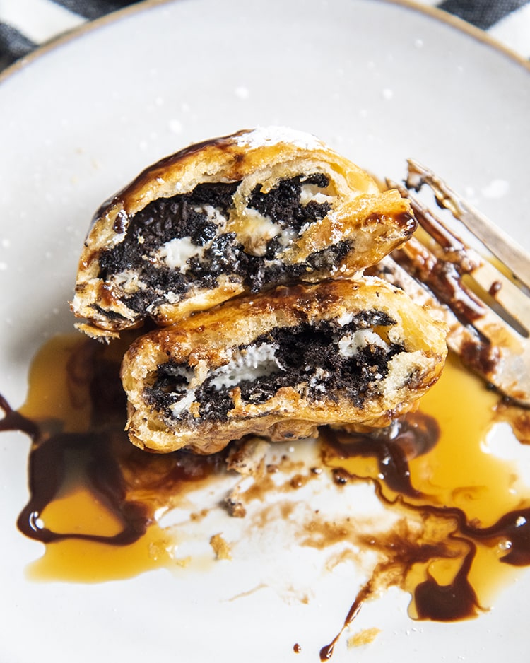 An air fried Oreo cut in half on a plate in a pile of caramel sauce and chocolate syrup.