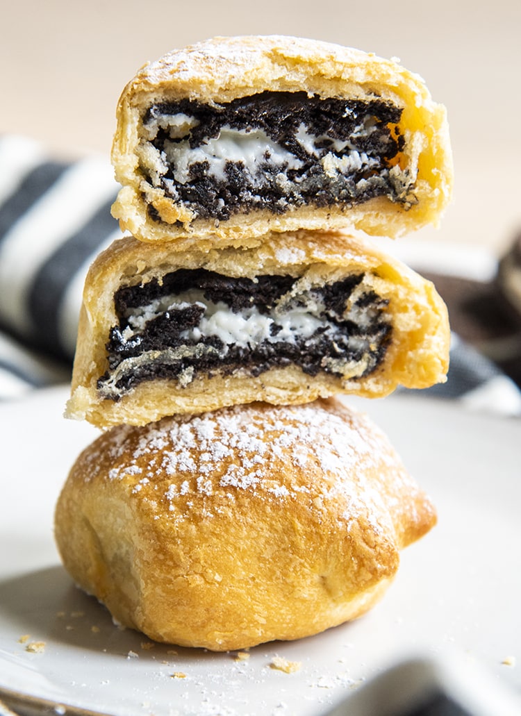An air fryer fried Oreo on a plate, with another on top that is cut in half with both halves stacked, and the Oreo in the middle is shown.