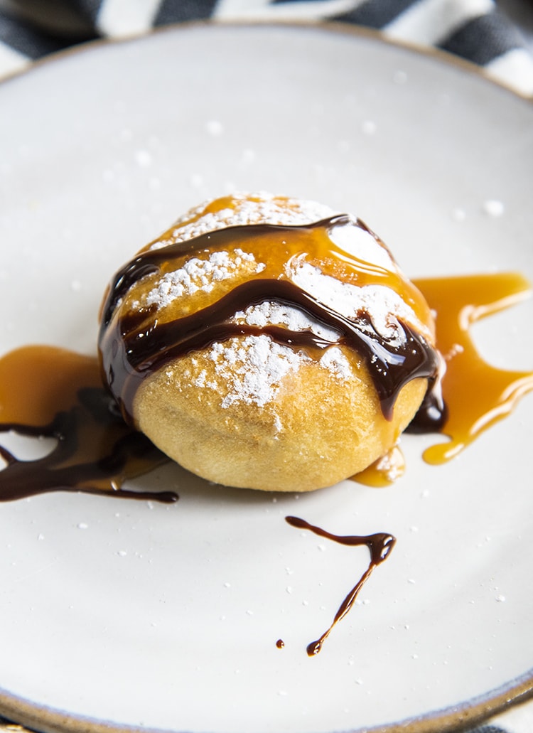 An air fried Oreo on a plate showing the dough, covered in powdered sugar, and drizzled with caramel and chocolate syrup.