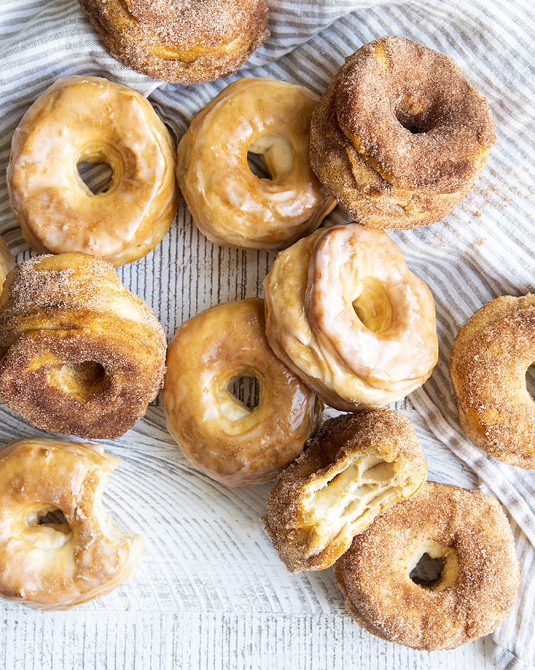 A pile of glazed and cinnamon sugar homemade donuts on a tea towel.