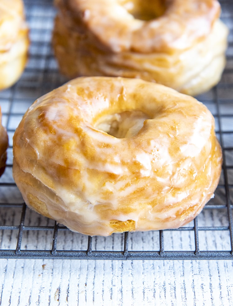 A close up of a homemade glazed donut on a cooling rack.