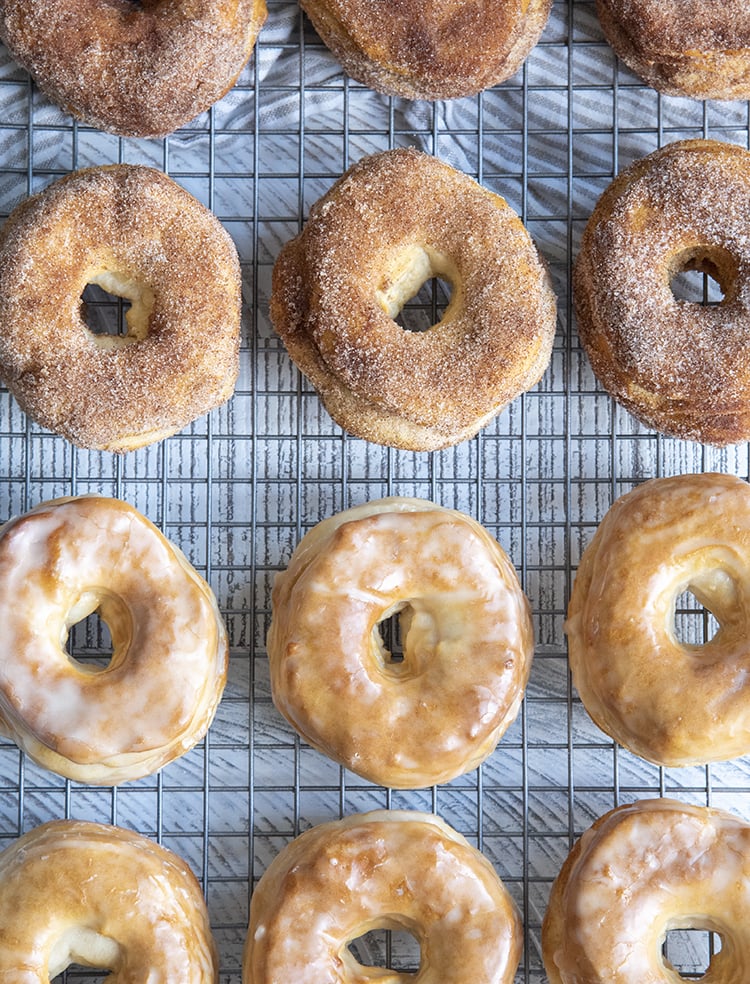 Cinnamon sugar and glazed donuts arranged in rows on a cooling rack.