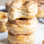 A stack of three air fryer donuts covered in a vanilla glaze. The top donut has a bite out of it showing flaky layers.