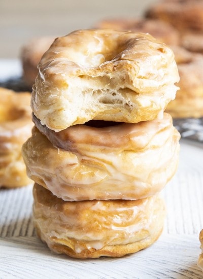 A stack of three air fryer donuts covered in a vanilla glaze. The top donut has a bite out of it showing flaky layers.