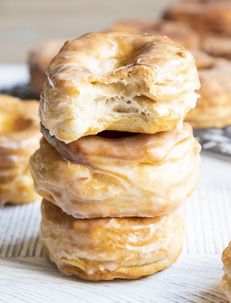 A stack of three air fryer donuts covered in a vanilla glaze. The top donut has a bite out of it showing flaky layers.