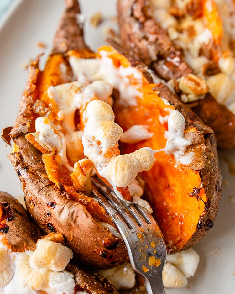 A close up of a baked sweet potato full of brown sugar, toasted marshmallows and pecans.