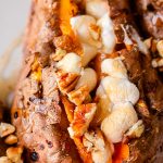 A close up of a baked sweet potato full of brown sugar, toasted marshmallows and pecans, with maple syrup drizzled over the top.