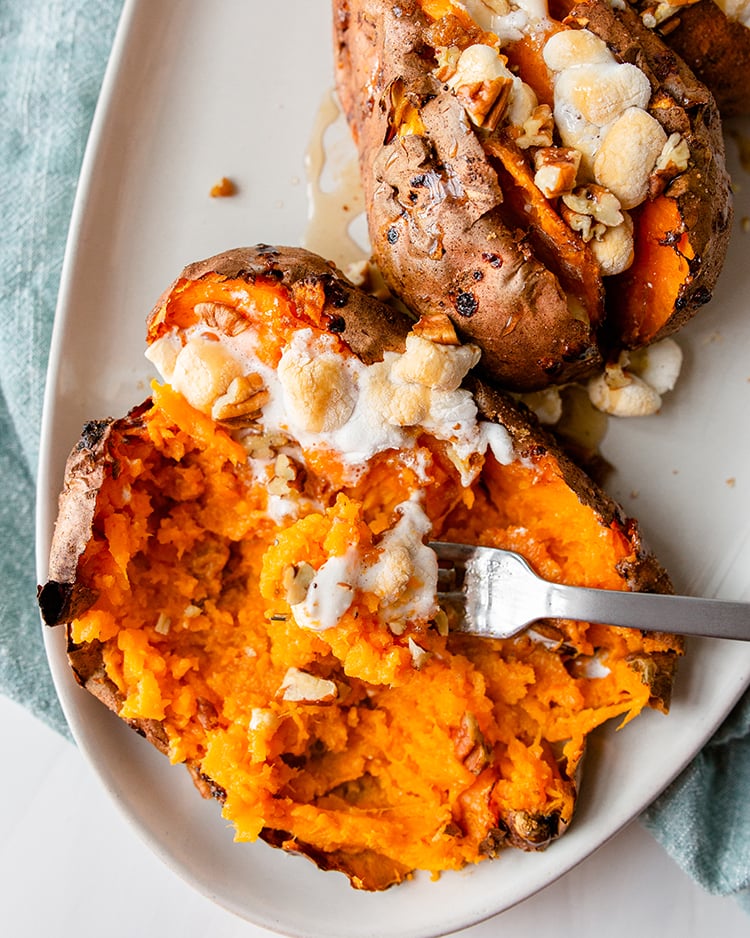A twice baked sweet potato that is being deconstructed with a fork, it is topped with pecans and toasted marshmallows.