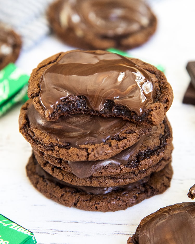 A stack of chocolate cookies, each topped with a melted chocolate Andes mint on top. The top mint is still melty.