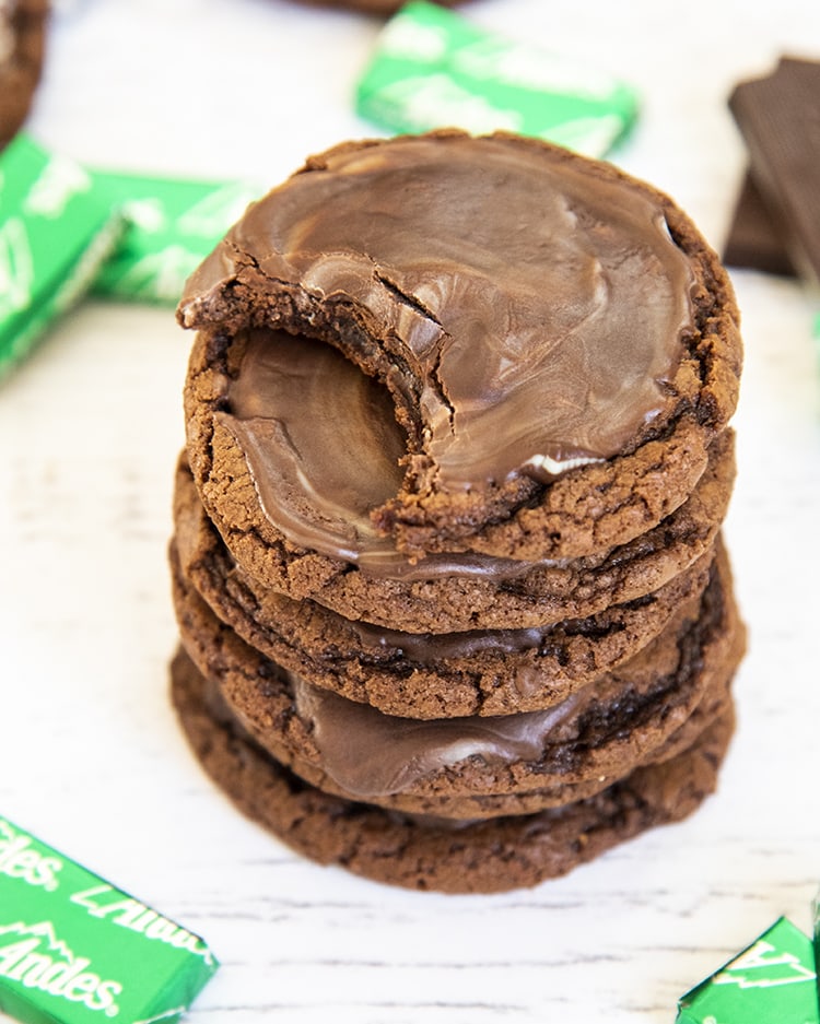 A stack of 6 chocolate cookies with a minty chocolate ganache on top. The top cookie has a bite out of it.