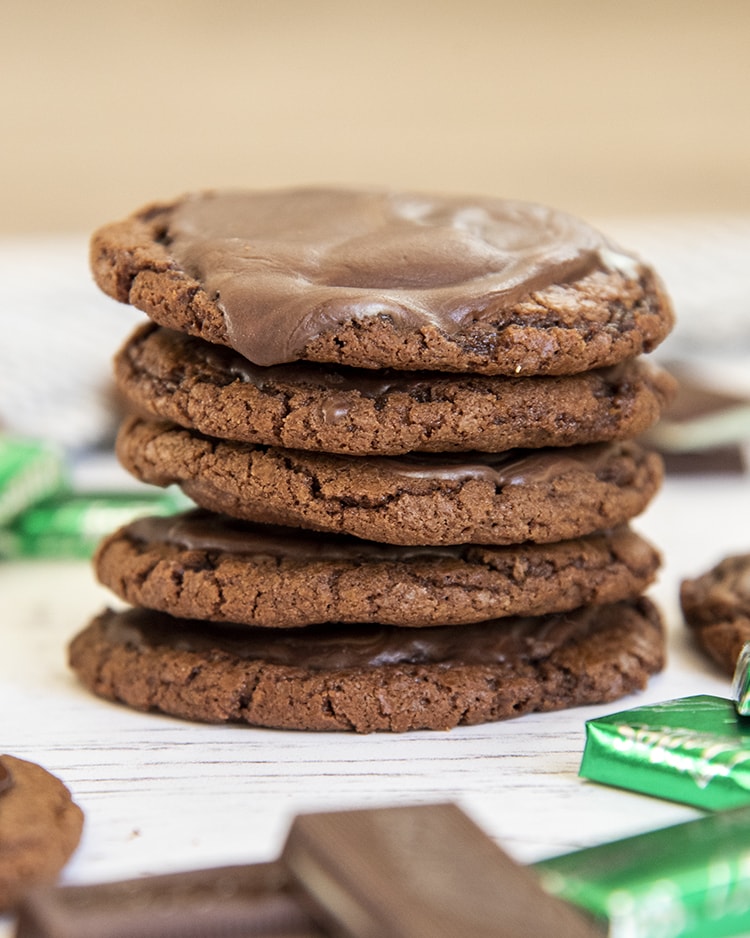 A stack of chocolate cookies, 5 cookies high. The top cookie looks like it has chocolate ganache on it.