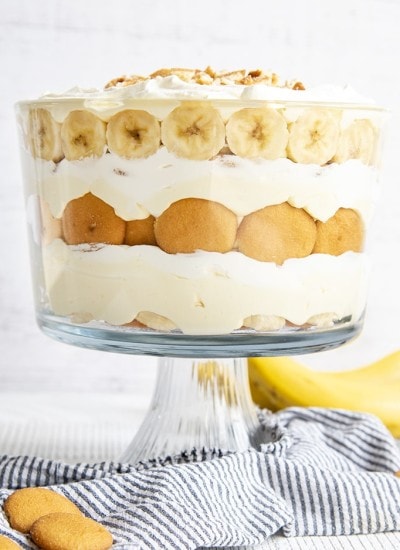 A layered banana pudding trifle in a trifle dish, with layers of Nilla Wafers, Banana Slices, Vanilla Pudding, and Whipped Cream.