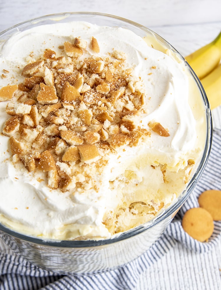 A banana pudding trifle with a serving scooped out of it, so you can see the yellow pudding underneath the top whipped cream layer.