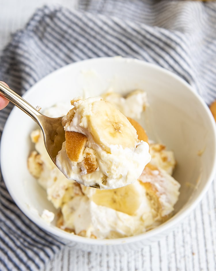 A bowl of banana pudding, with a spoonful of it being held above it.