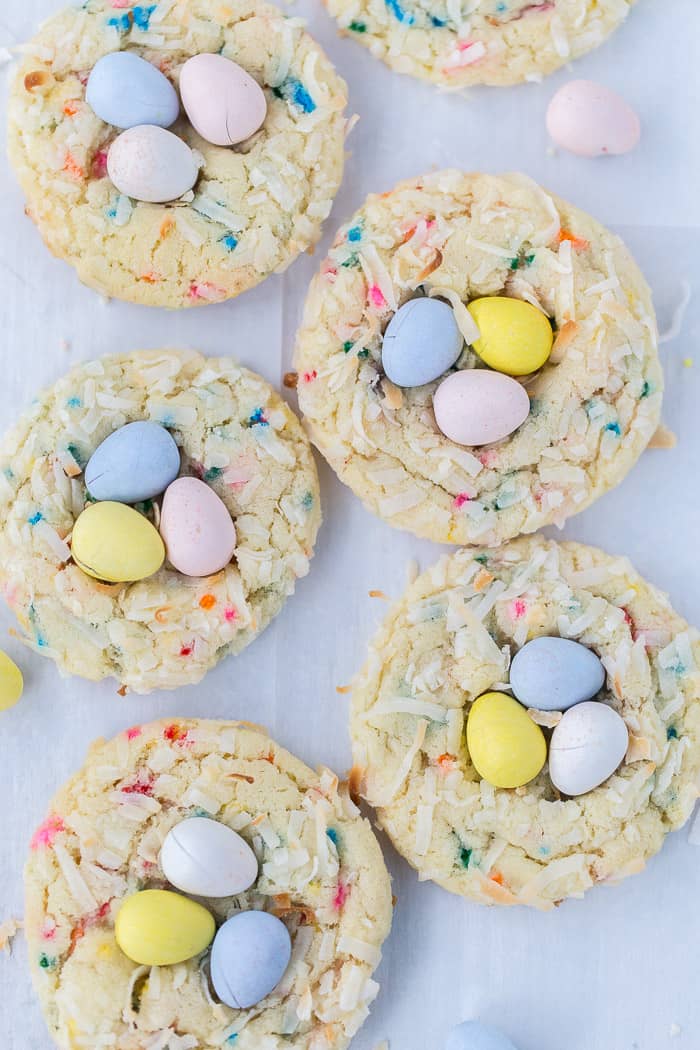 Cookies full of colored sprinkles, and covered in coconut, and topped with three pastel colored chocolate candies.