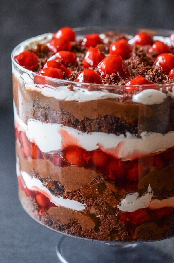 A half of a trifle dish showing layers of chocolate cake, cherry pie filling, whipped cream, and chocolate pudding stacked all the way up to the top of the trifle dish.