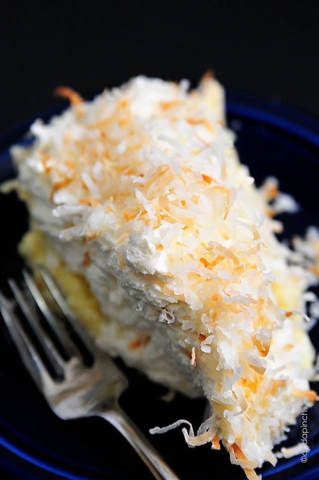 A close up of a slice of coconut cream pie on a blue plate topped with toasted coconut. 