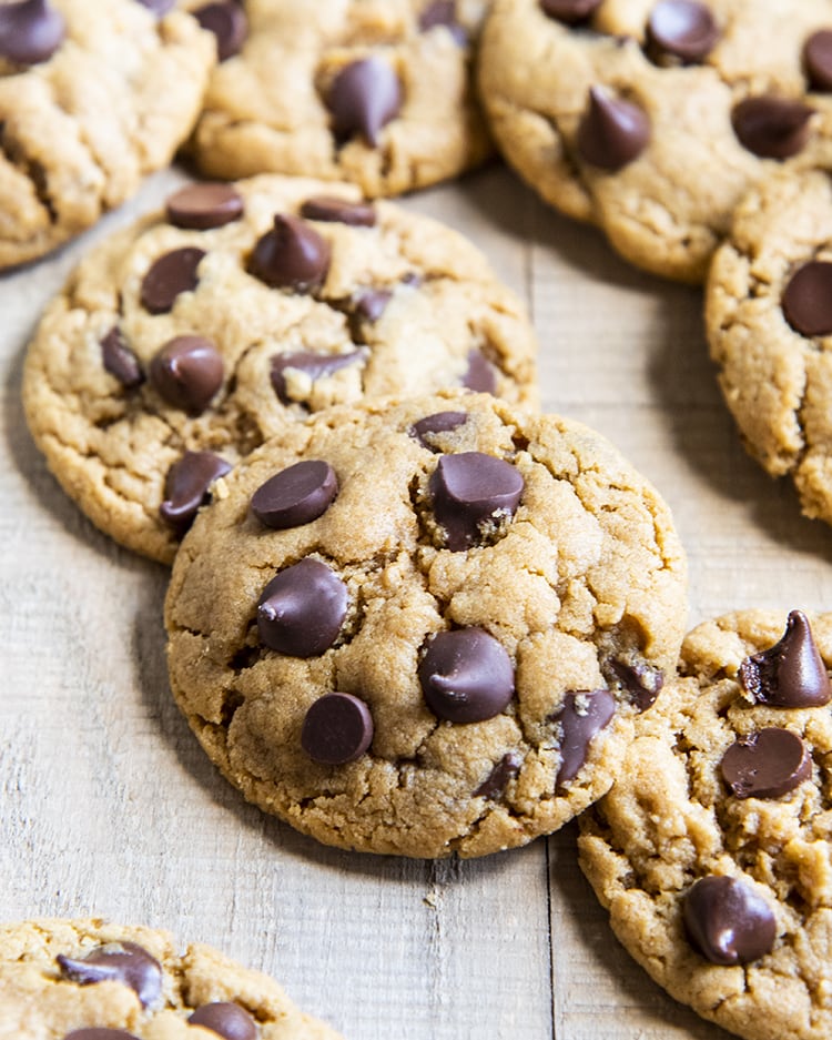 A close up of a cookie slightly resting on another cookie. The cookies are all topped with chocolate chips.
