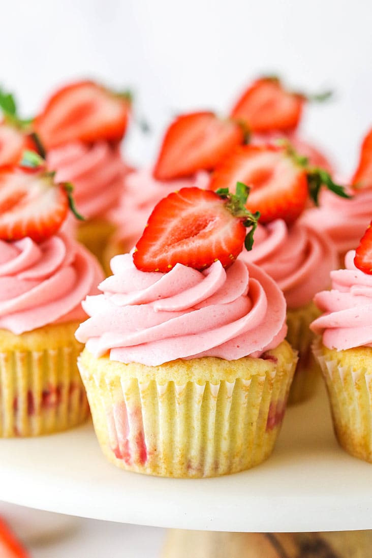 Strawberry cupcakes topped with a pink frosting, and half a strawberry each.