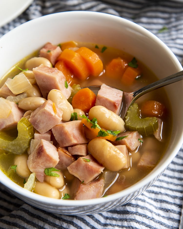 A close up of a bowl of ham and bean soup with celery and carrots.