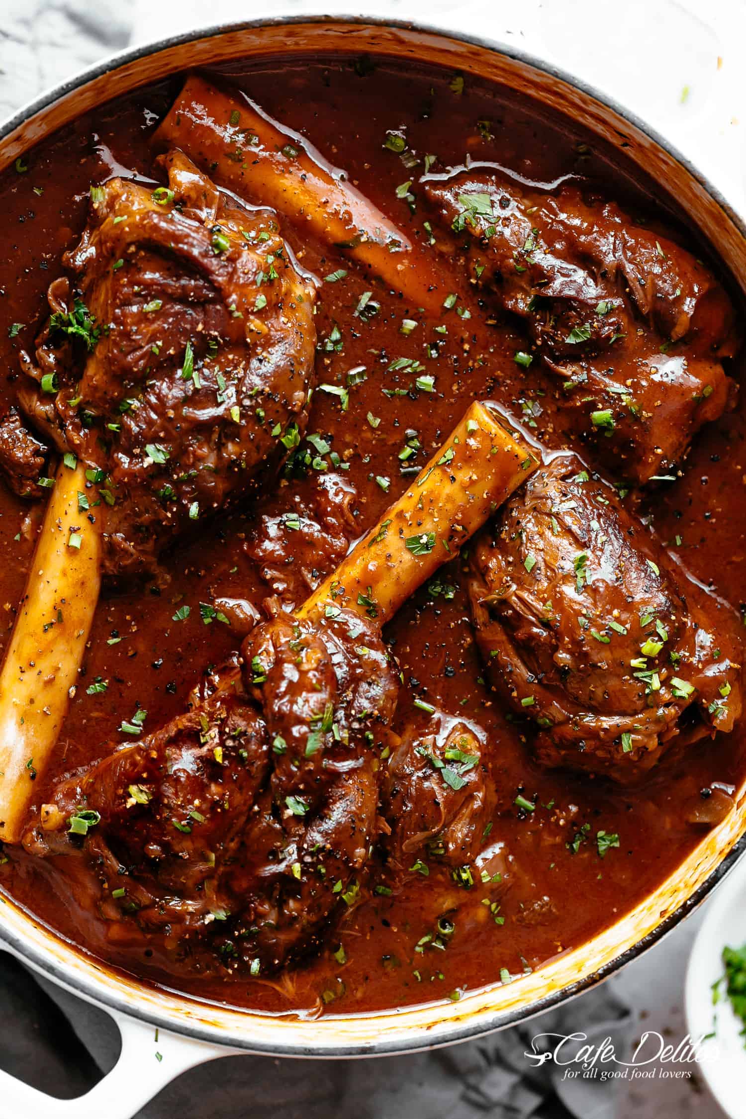 Lamb shanks in a pan in red wine sauce.