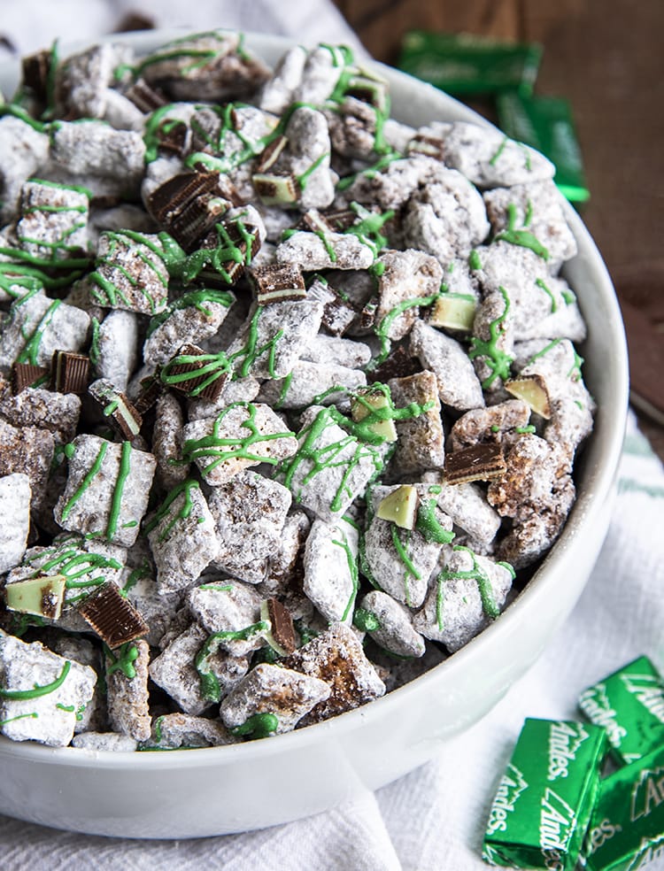 Mint Chocolate Muddy Buddies in a white bowl. They are drizzled with green candy melts over the top.